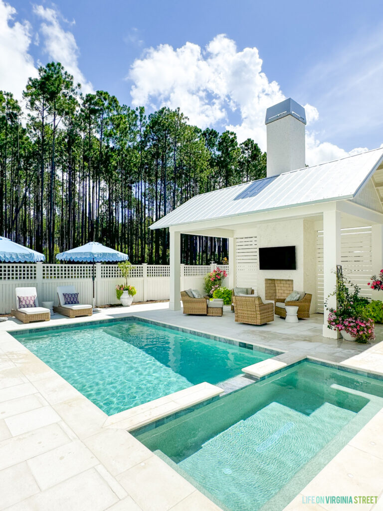 Life On Virginia Street pool details including pebble tec color, pavers, outdoor furniture and more. Includes a white pool cabana, outdoor lounge chairs, colorful flowers, and a light blue swimming pool.