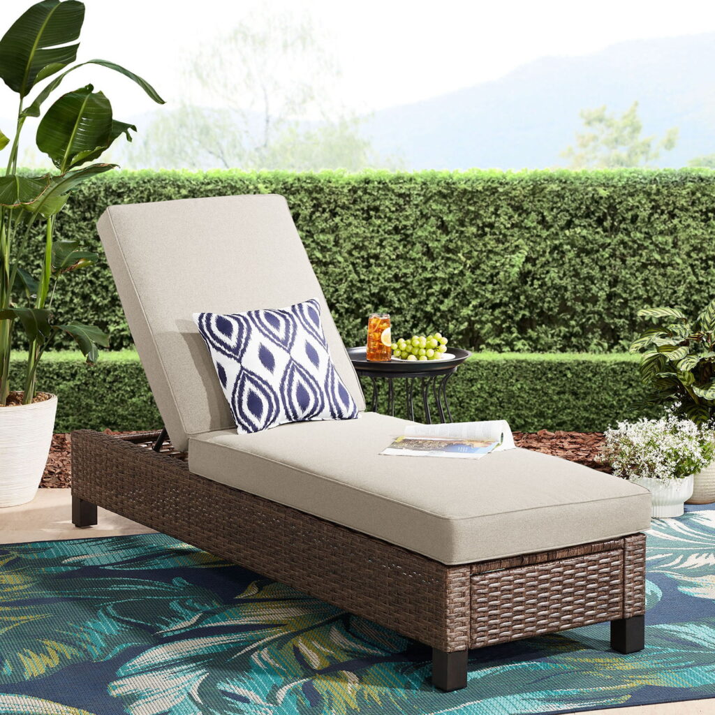 Adjustable pool lounge chair with a wood wicker frame and beige cushion styled with a navy blue and white outdoor pillow.