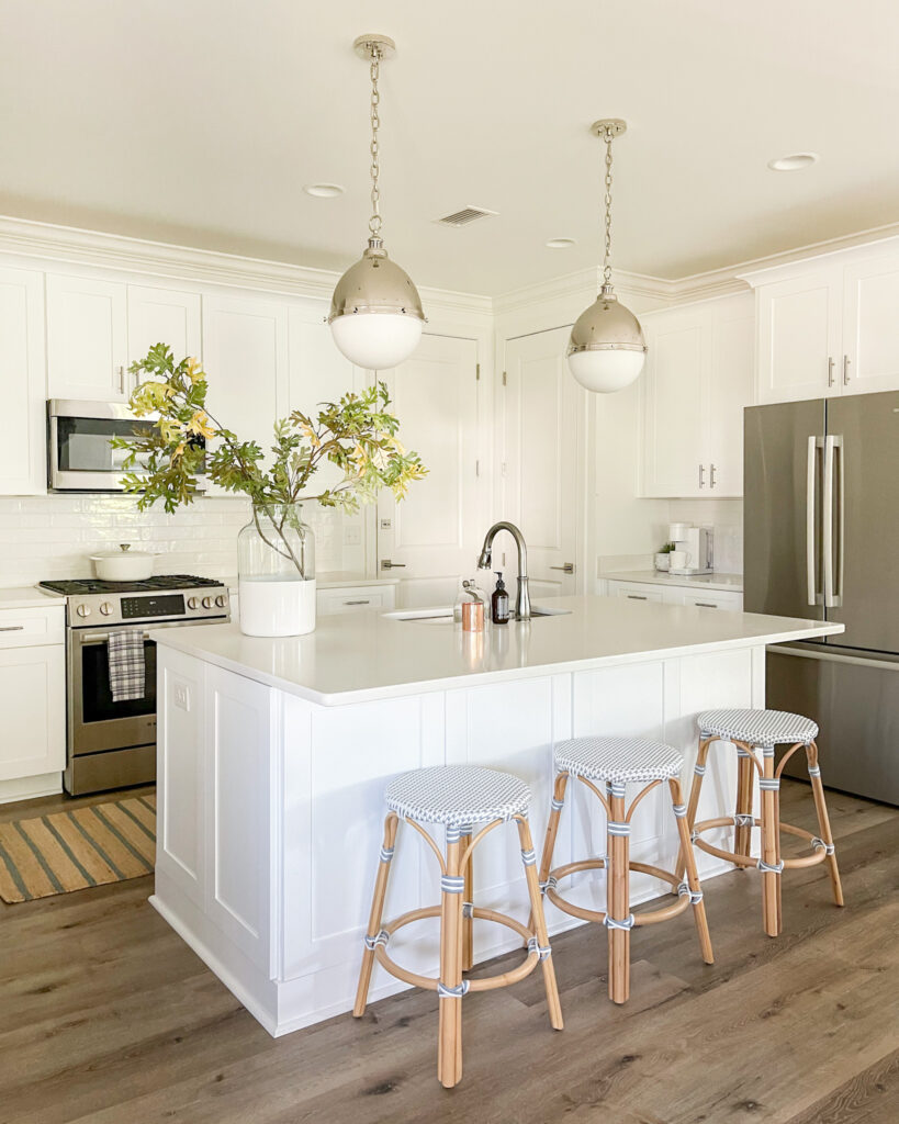 A Florida coastal cottage kitchen with round pendant lights, woven bistro backless counter stools, a striped jute rug and oak leaves.