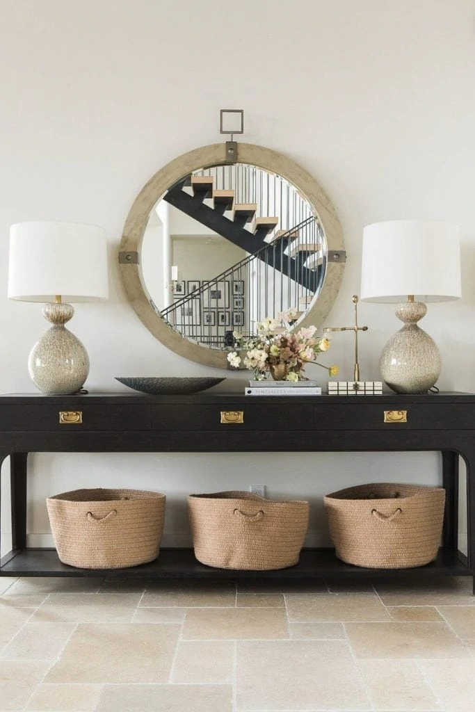 A white wall with a hallway table in front of it and a large round mirror on the wall above the table.